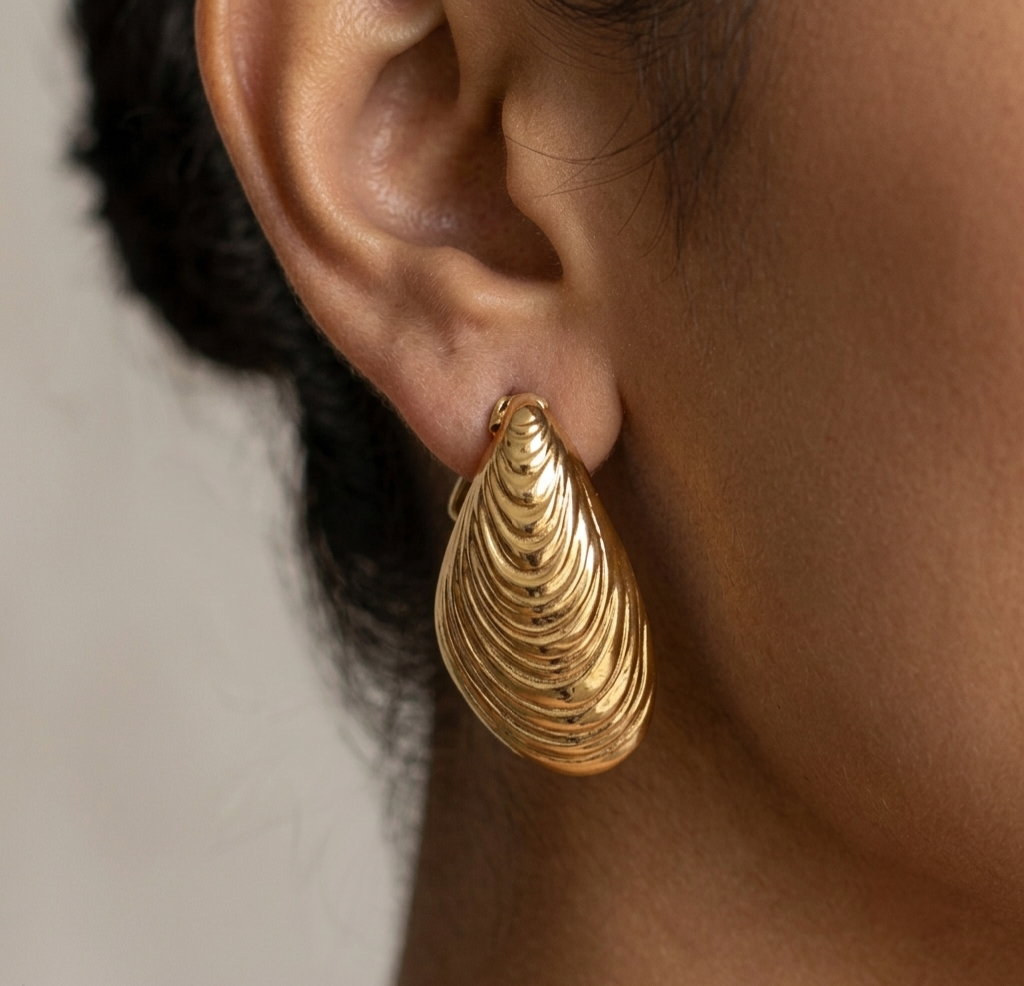 Gold teardrop earring worn by a person with a neutral background