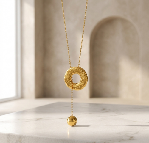 Gold necklace with a textured pendant on a marble surface